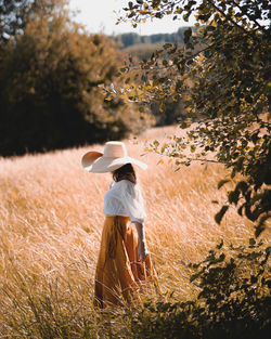 Woman standing in the field wearing dress and a hat