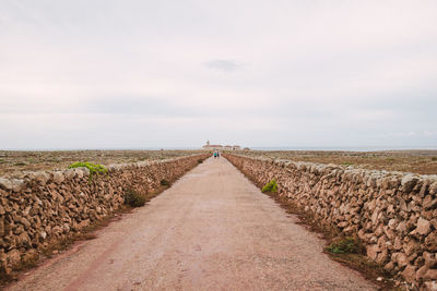 Road leading towards agricultural field against sky