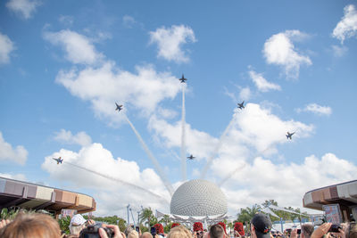 Low angle view of crowd looking at airshow against cloudy sky