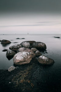 Pebbles on rocks by sea against sky