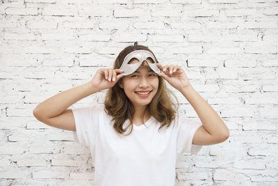 Portrait of smiling young woman wearing mask while standing against wall