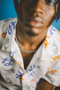 Serious african american male with braided hairstyle and bright makeup looking at camera with folded hands on blue background in studio
