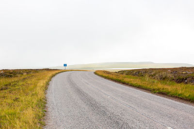 Road amidst field against clear sky