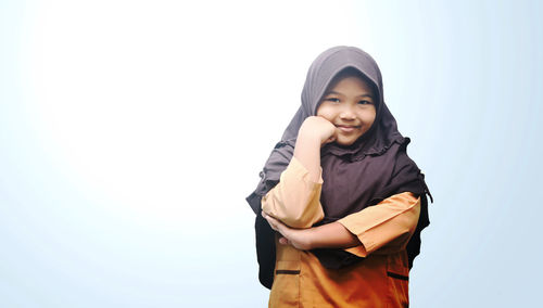 Portrait of happy girl wearing hijab while standing against clear sky