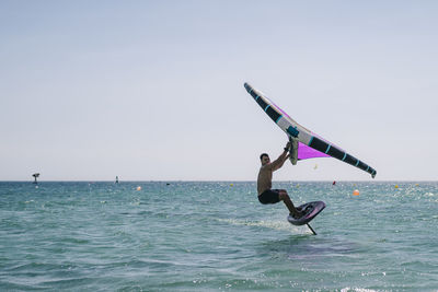 Young shirtless man practicing wind foil in sea