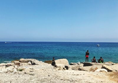 Scenic view of sea with people at beach against clear sky