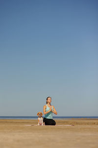 Rear view of woman sitting on beach against clear sky