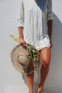 Midsection of man holding hat standing against wall