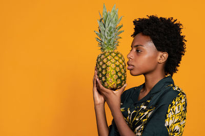 Young african american woman with short hair dressed in a summer shirt posing with pineapple