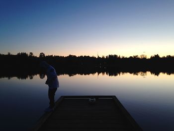 Silhouette man standing by lake against clear sky