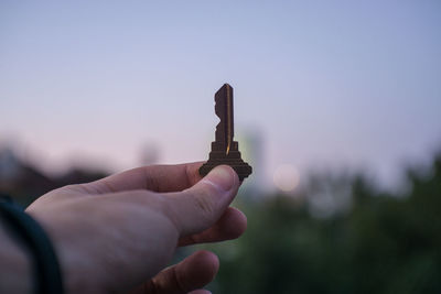 Close-up of hand holding key against sky