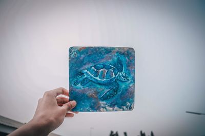 Close-up of hand holding painting against blue wall