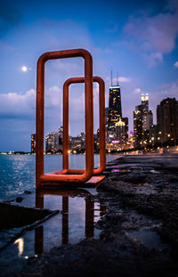 Illuminated buildings by sea against sky at dusk