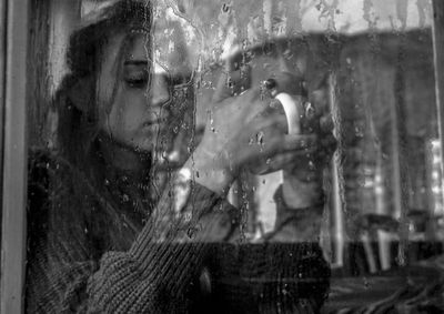 Portrait of woman seen through wet window during rainy season