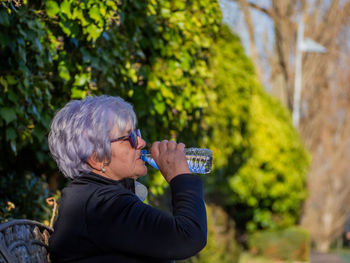 Side view of senior woman drinking water from bottle in park