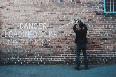 Man holding sunglasses in front of brick wall