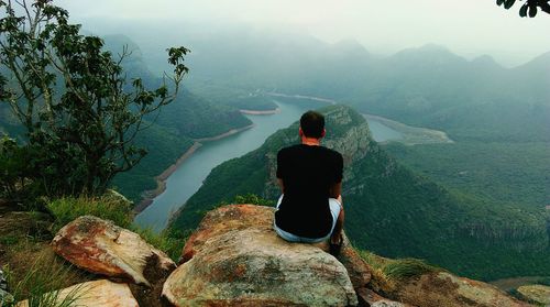 Rear view of man sitting on rocks against lake