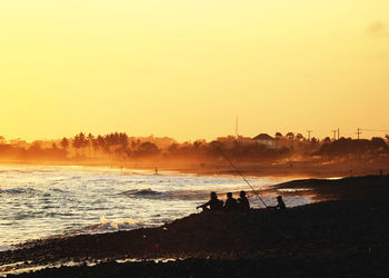 Silhouette people on beach against sky during sunset