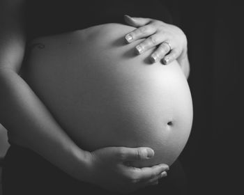 Midsection of woman touching face against black background