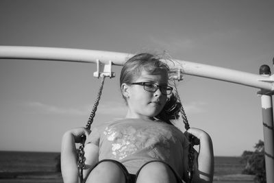 Girl swinging against sky during sunny day