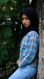 Young woman wearing hijab standing by wall