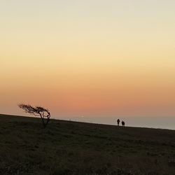 Silhouette people walking at beach against sky during sunset