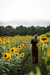 Rear view of woman on sunflower field against sky