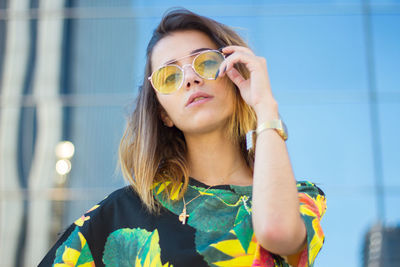 Fashionable young woman wearing top and sunglasses in city