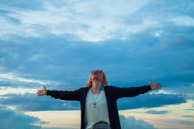 Young man with arms outstretched standing against sky