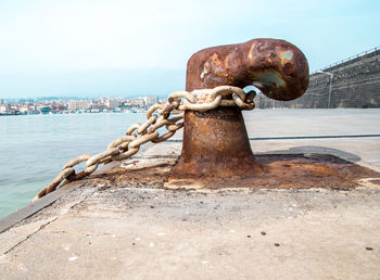 Close-up of rusty chain on harbor against sky