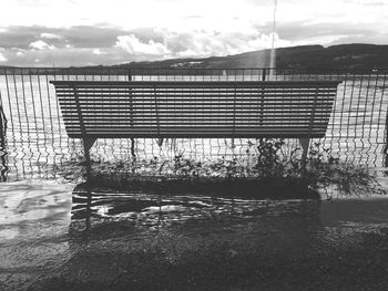 Empty bench by lake against sky