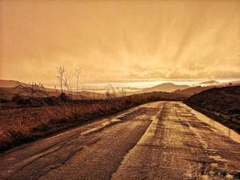 Road amidst field against sky during sunset