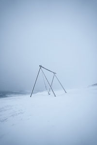 View of swing on snow covered land against sky