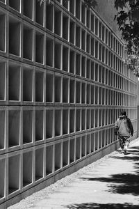 Rear view of man walking on footpath against building