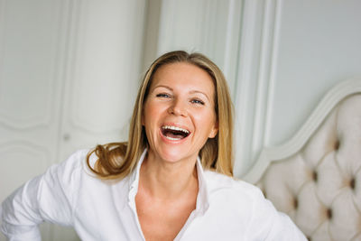 Friendly charming blonde woman with long fair hair in casual clothing sitting on the bed in bright 