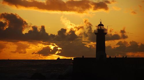 Silhouette lighthouse by sea against sky during sunset