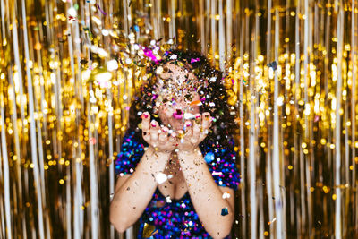 Portrait of woman blowing confetti against tinsel