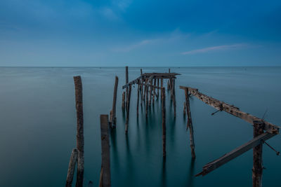 Wooden posts in sea against sky