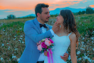 Smiling bride and groom with bouquet romancing on field