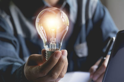 Midsection of businessman holding illuminated light bulb in office