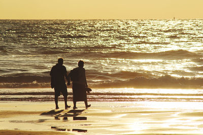 Rear view of men on beach against sky during sunset