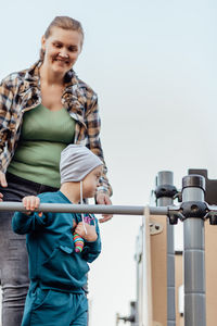 A boy, person with down syndrome walks in the park with his mother, going down the children's slide