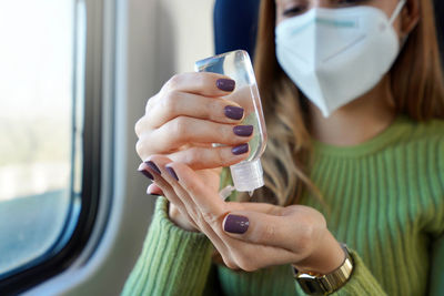 Business woman with medical face mask using alcohol gel sanitizing hands on public transport. 