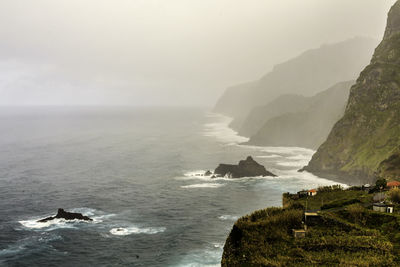 Scenic view of sea by rocky mountains against sky