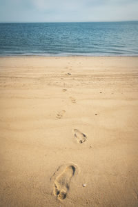 Footprints on sand at beach against sky