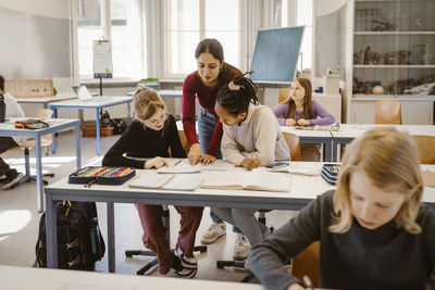 Teacher explaining male and female school students sitting at desk in classroom