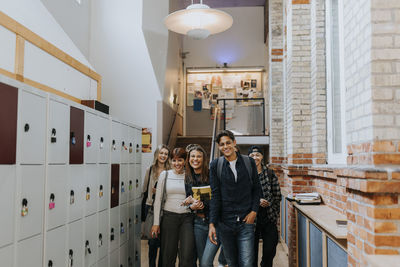 Portrait of happy male and female students walking by lockers in corridor