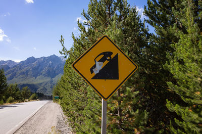 Road sign by trees against sky