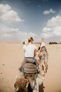 Rear view of woman riding motorcycle on desert against sky