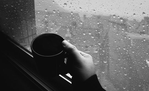 Person holding wet glass window with rain drops